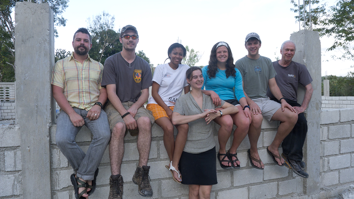 A group photo of 7 faculty and students from the University of Tennessee sitting on a masonry wall.