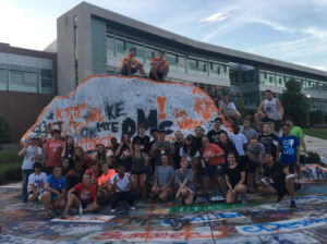 A large group of high school students with the famous UT rock painted with DMC for Design Matters! Camp.